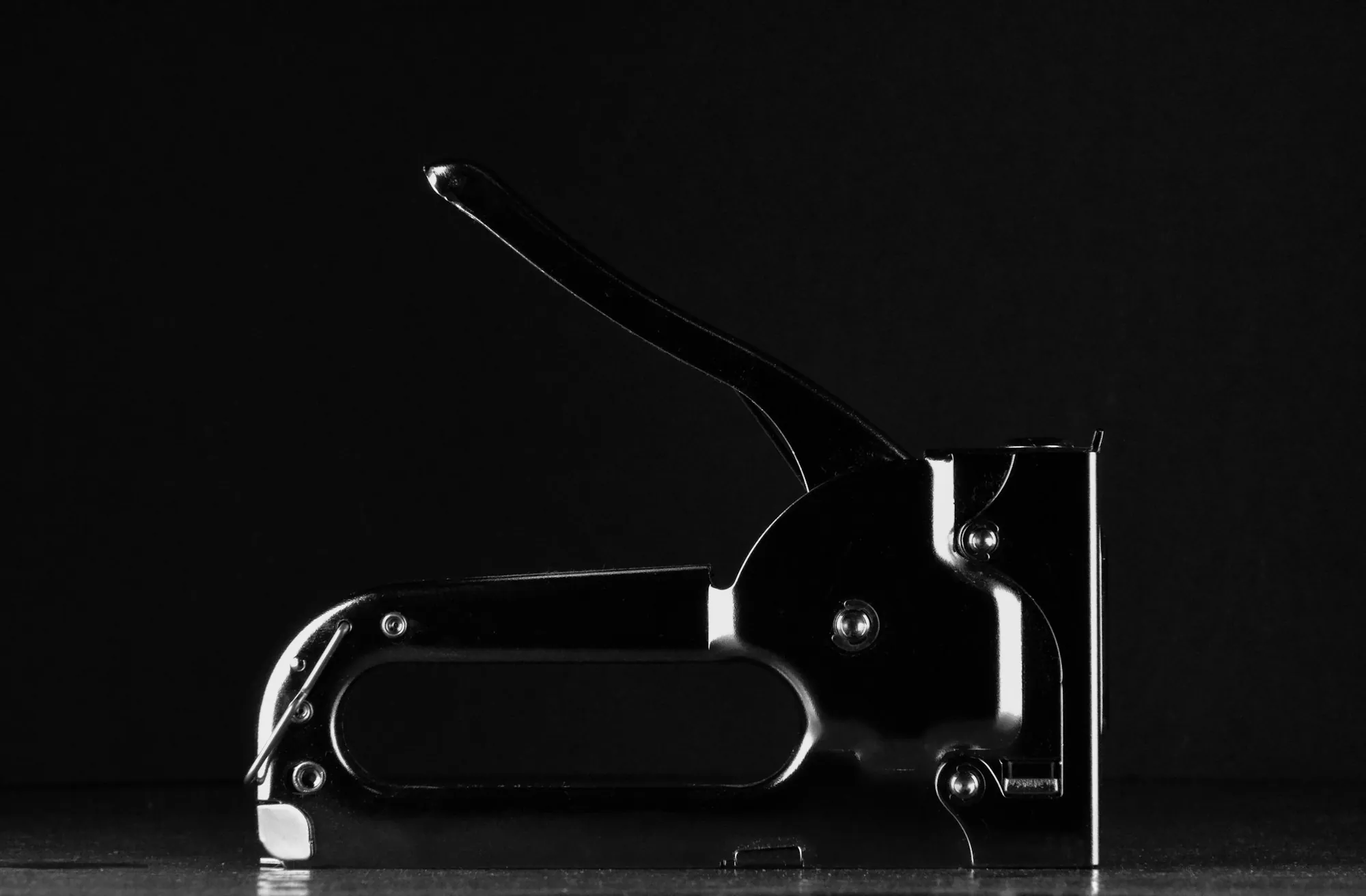 Black hand staple gun on a dark background, a tool used to fasten roof underlayment before ice-and-water shield and shingles go on a Decatur roof