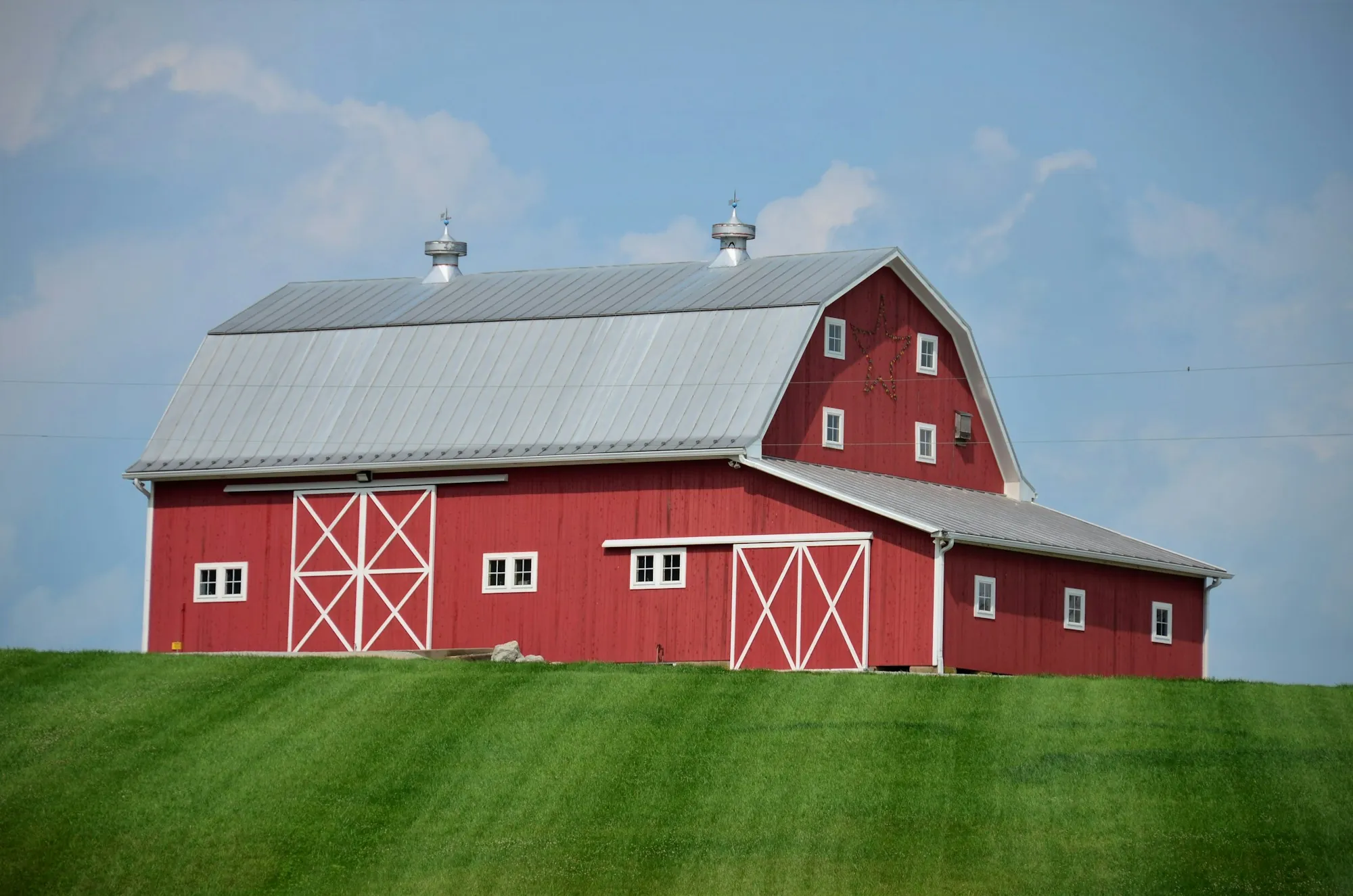 Red barn with a silver metal roof on a green lawn