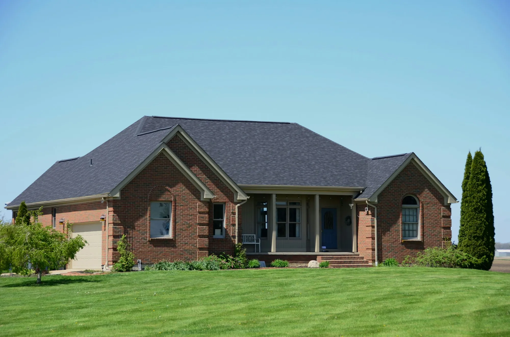 Brick ranch home with a dark hipped shingle roof and green lawn