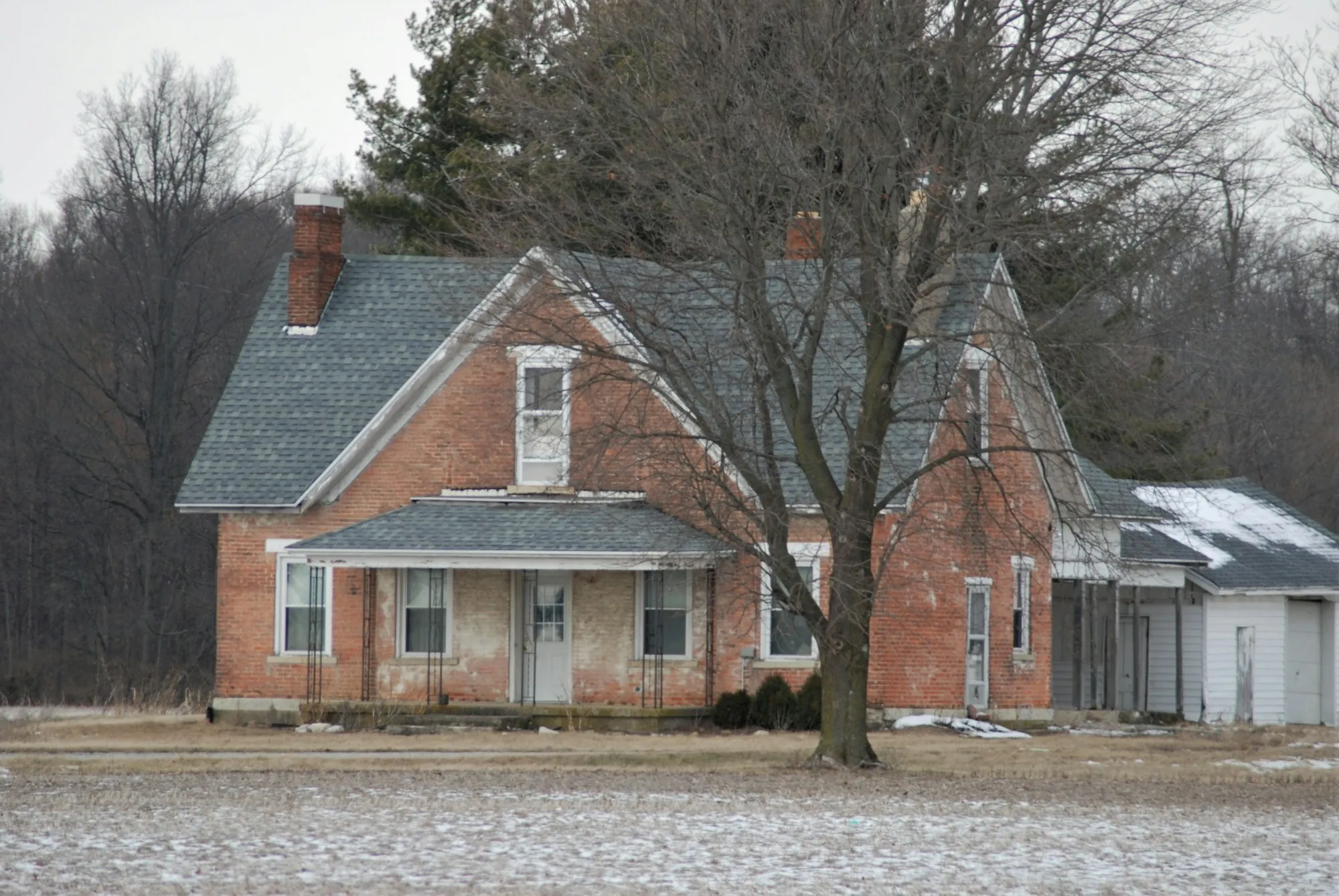 Old brick farmhouse beside bare winter trees